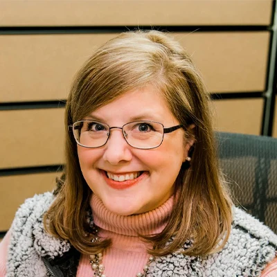 scheduling coordinator, Amy E. is seen sitting at her desk smiling warmly at the viewer