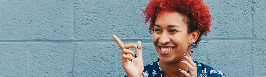 Dentist LaGrange GA Cosmetic Dentistry Focused happy gorgeous smiling woman with curly bright red hair pointing