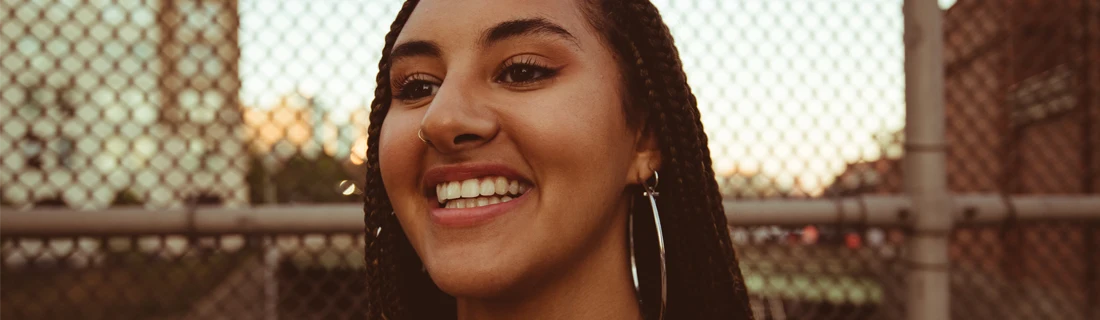 Dentist LaGrange GA Dental Crowns Focused woman with tiny braids and huge hoop earrings is smiling and looking off to the left