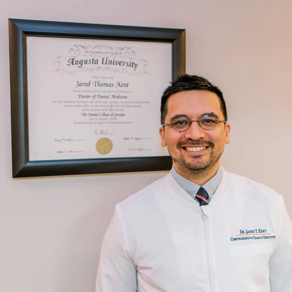 a photo of Dr. Jared Kent standing in front of his framed doctorate diploma